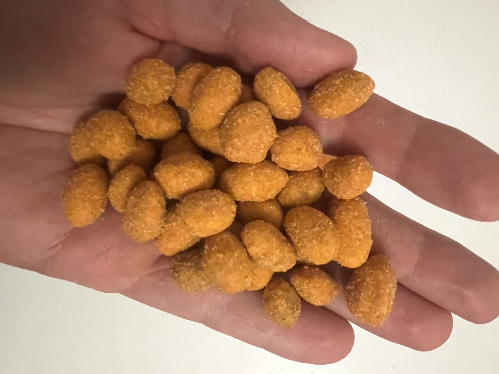 Handful of crunchy orange paprika-coated peanuts showing the sizes and shapes