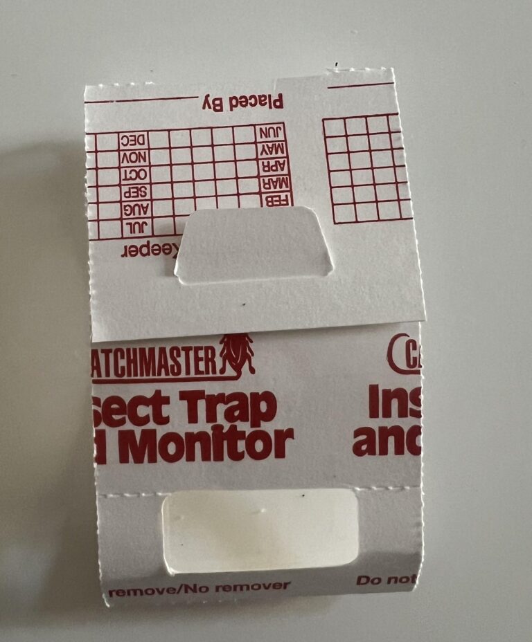 Original photograph of a folded white Catchmaster Insect Trap and Monitor with red printing on a light surface