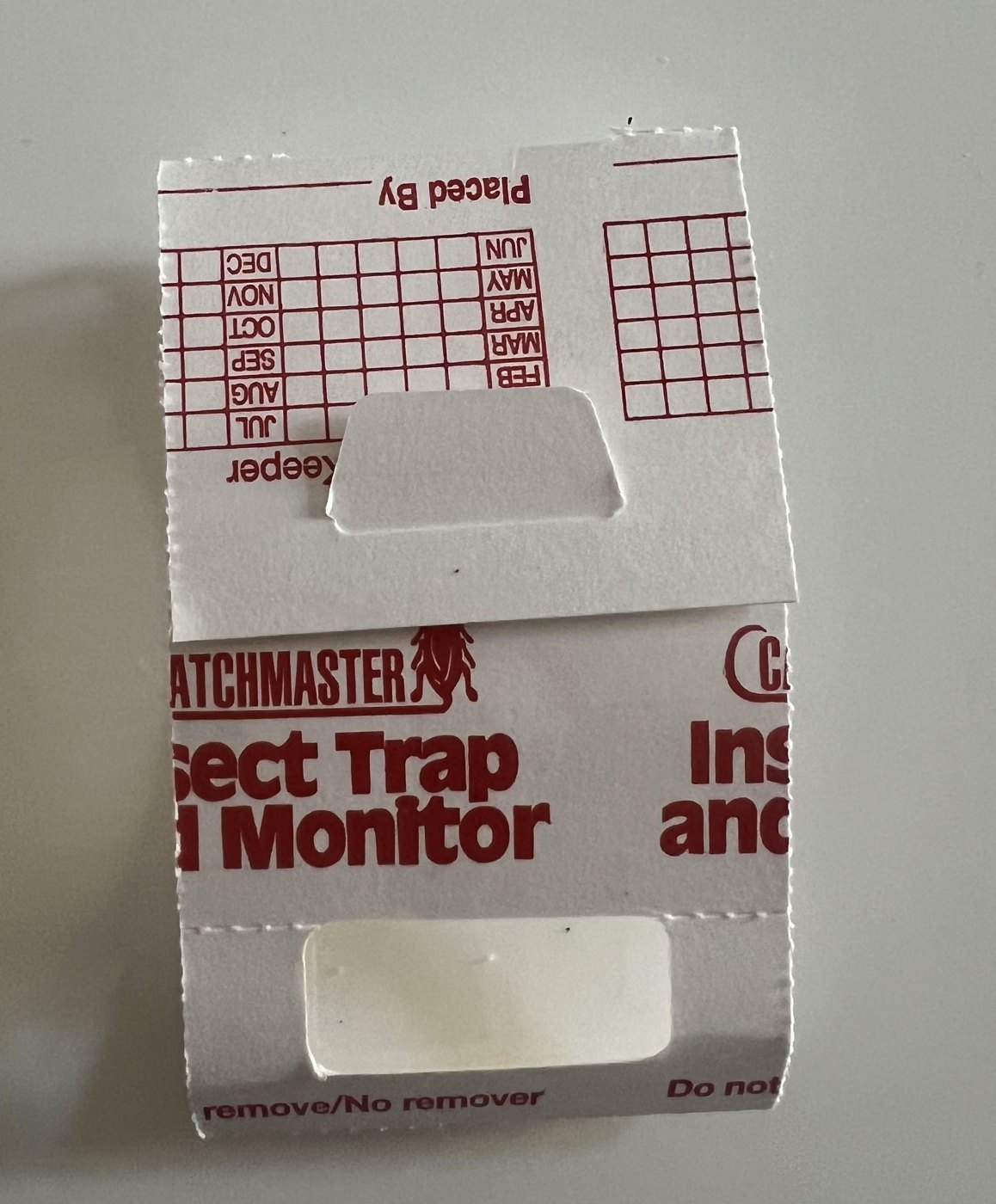 Original photograph of a folded white Catchmaster Insect Trap and Monitor with red printing on a light surface