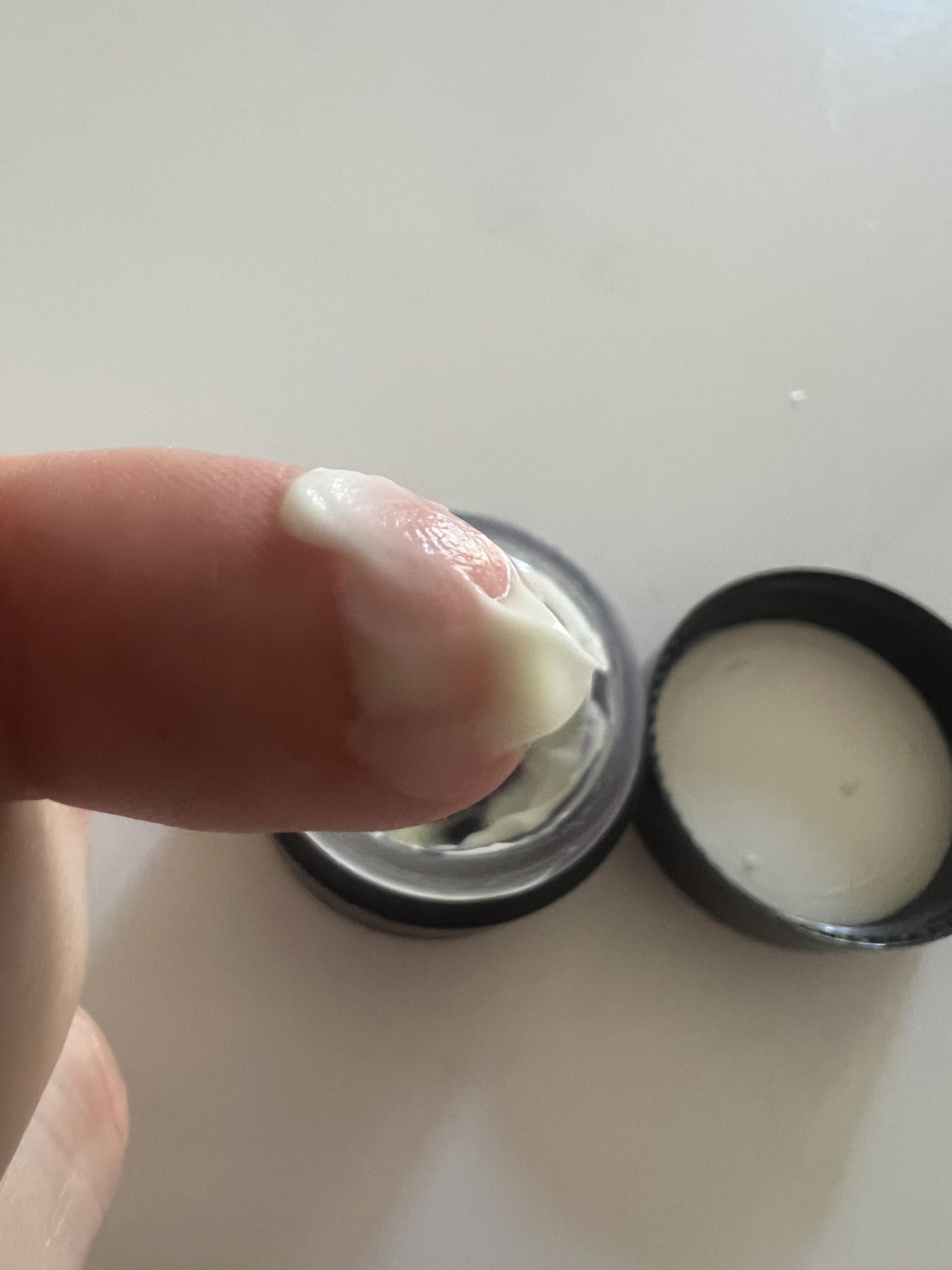 Small white dab of Eight Saints eye cream on fingertip above the open jar