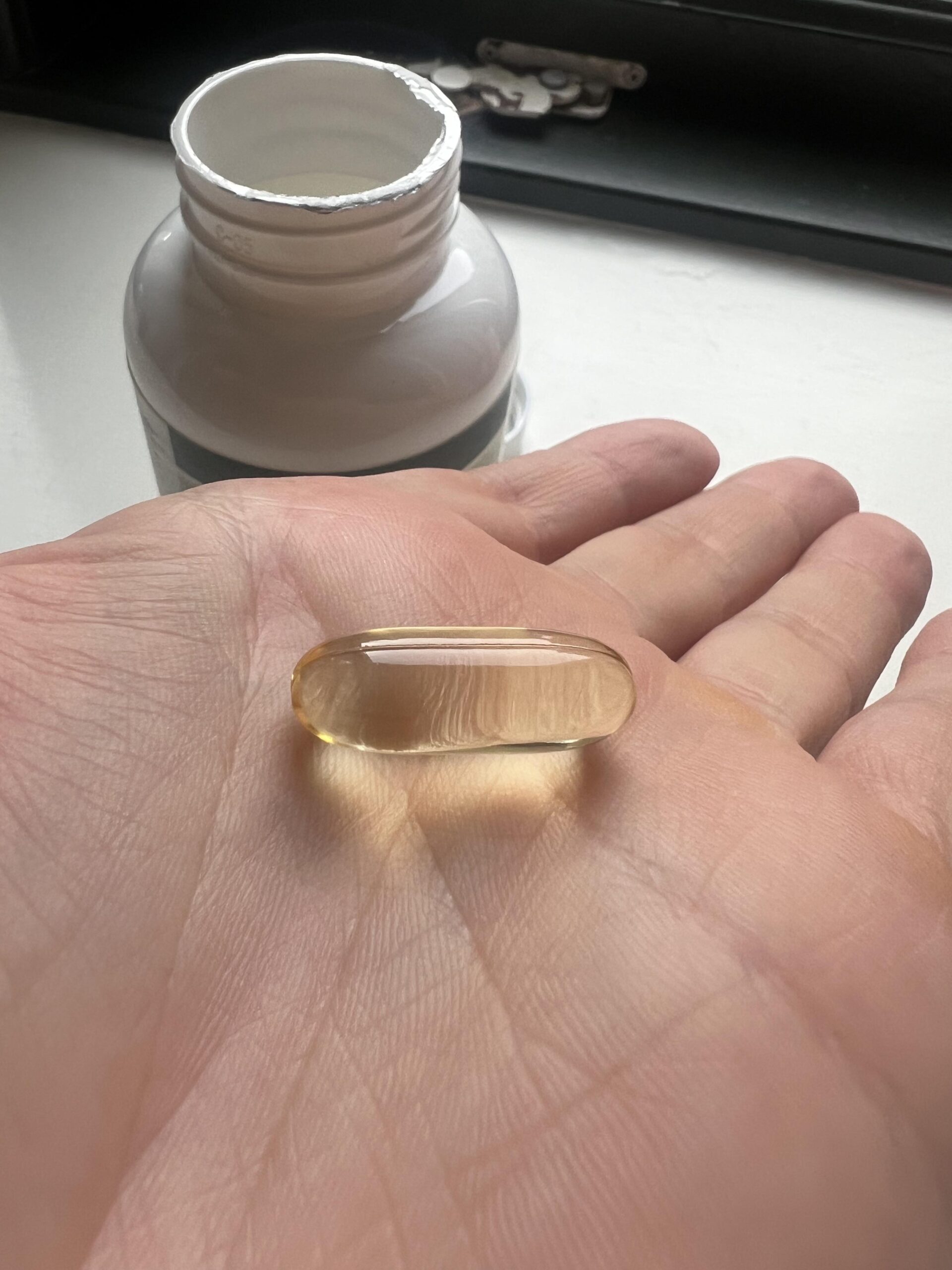 Single translucent golden EXVital algae omega-3 capsule displayed on an open palm