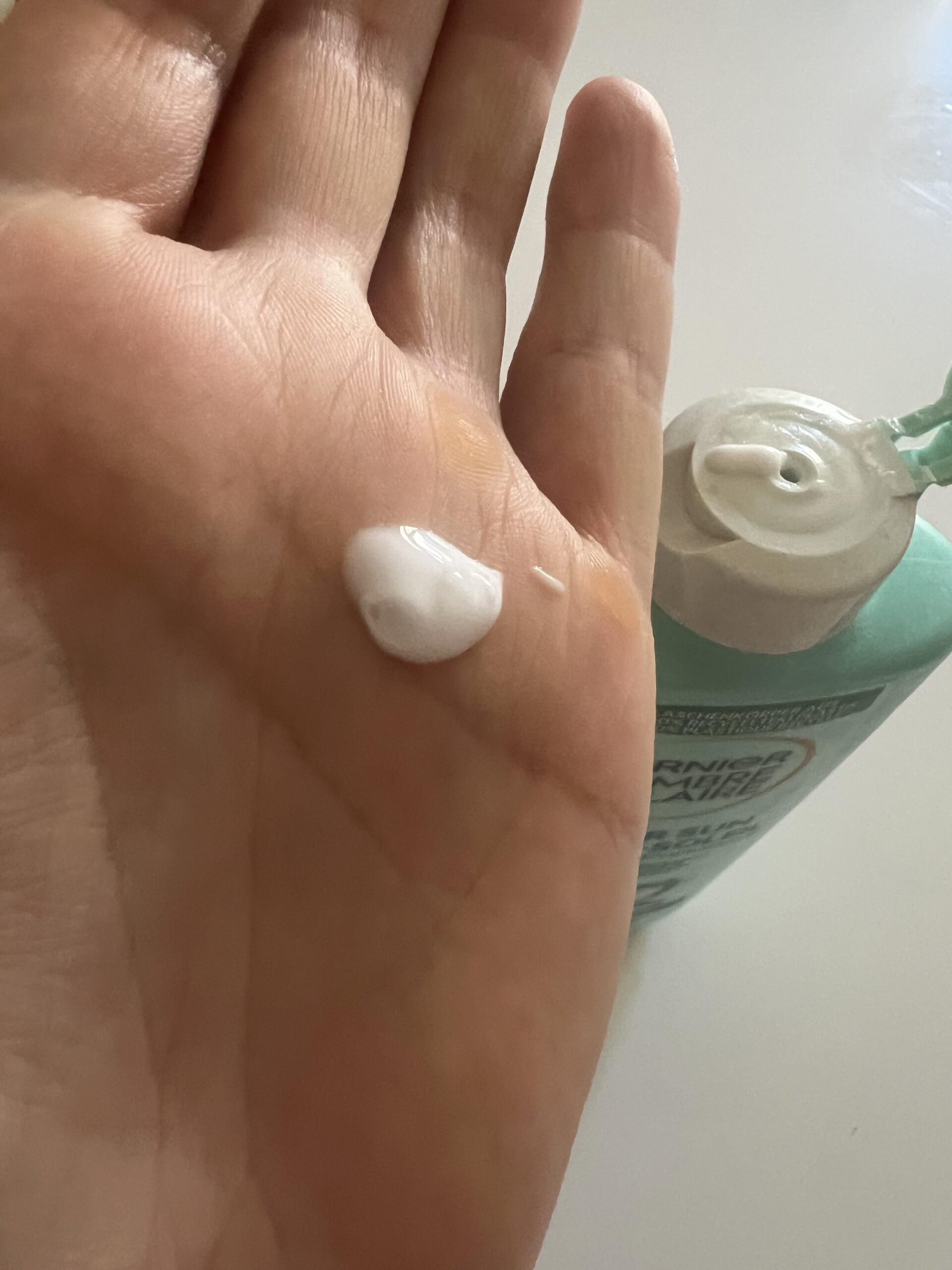 My original photograph of a small white dab of Garnier Ambre Solaire After Sun lotion on my palm, with the bottle's open cap nearby