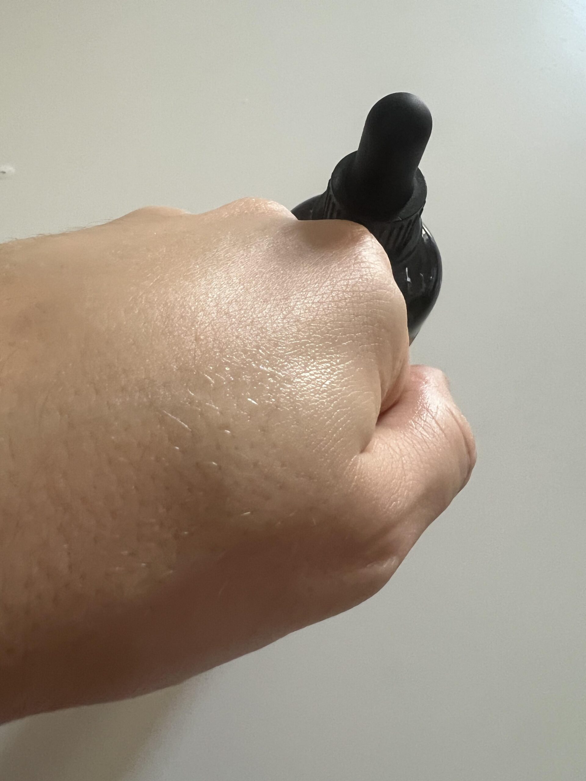 My original photo of the back of my hand after spreading Kapua Naturals azelaic acid serum, with its dropper bottle in the background