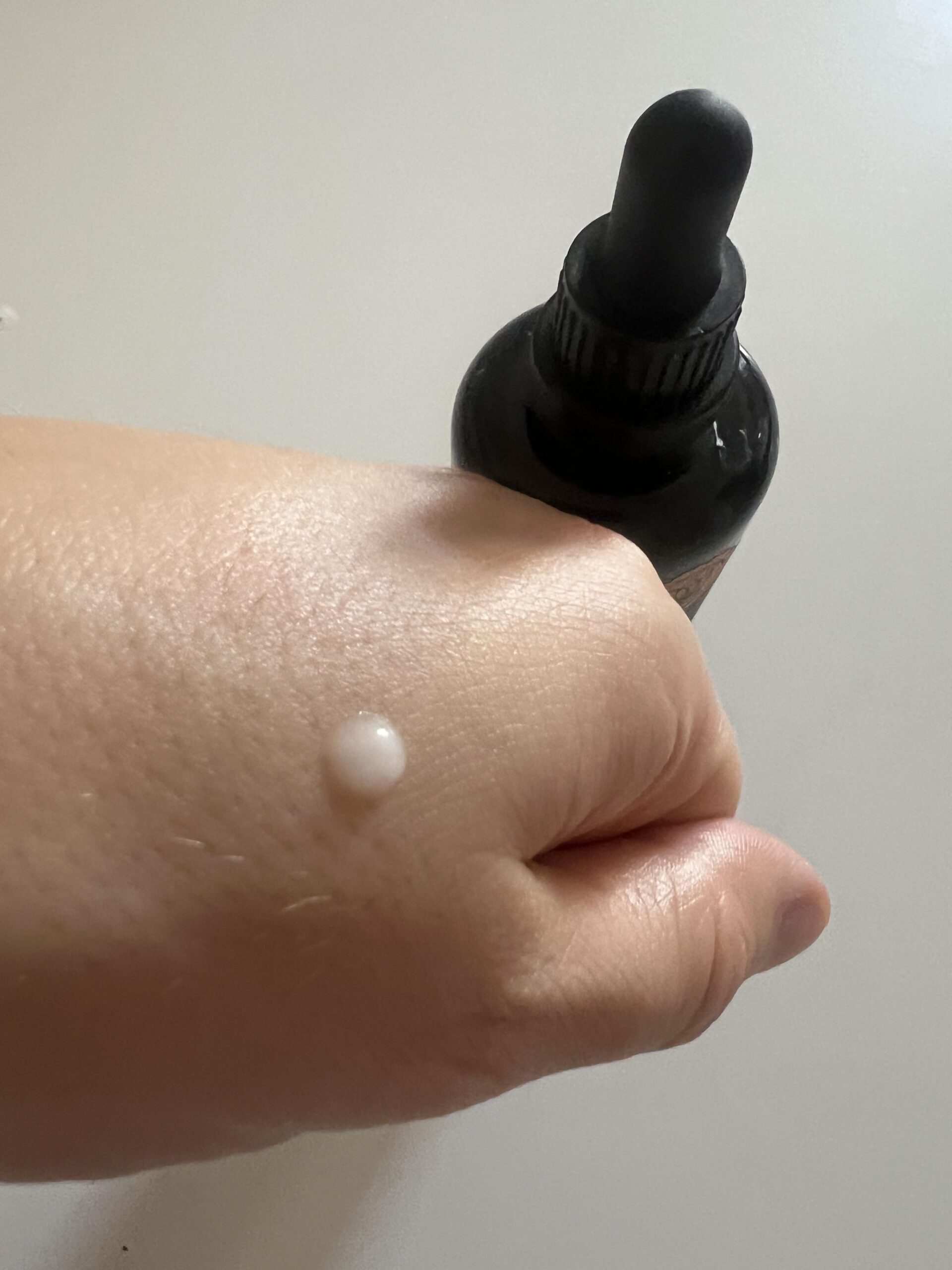 My original photo showing one small pale droplet of Kapua Naturals azelaic acid serum on the back of my hand next to its black dropper bottle