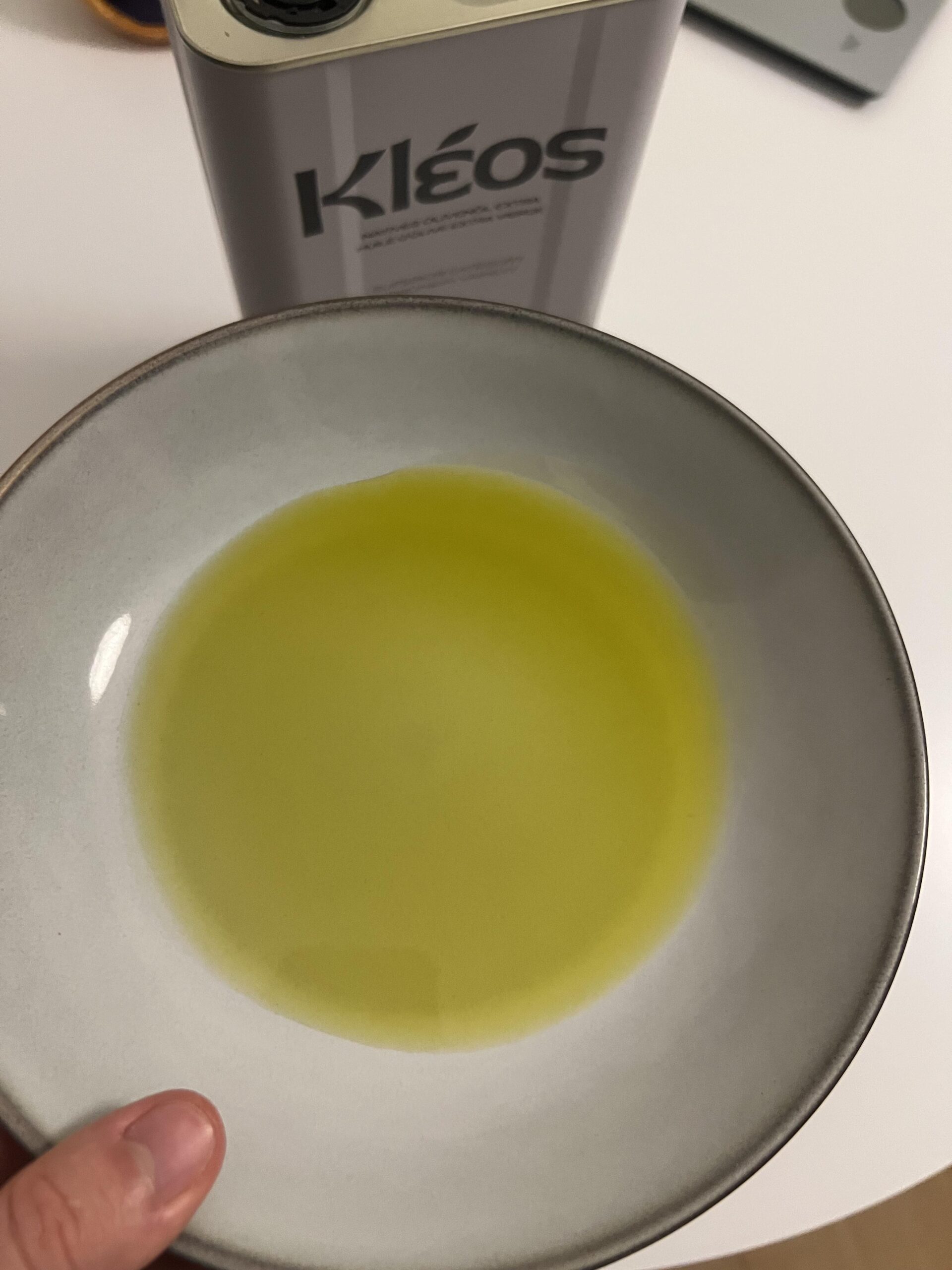 Golden Kleos extra virgin olive oil in a bowl, with the tin behind it