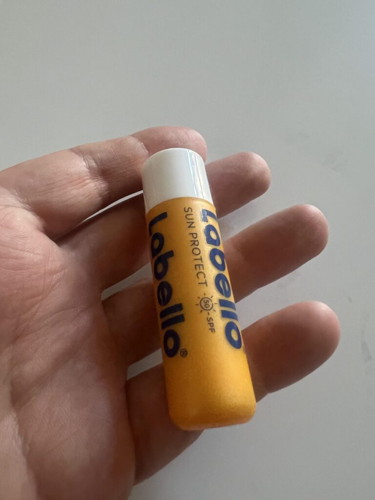 Original photo of the Labello Sun Protect SPF 50 4.8 g orange-and-white lip balm stick held upright in a hand, showing its front SPF 50 label