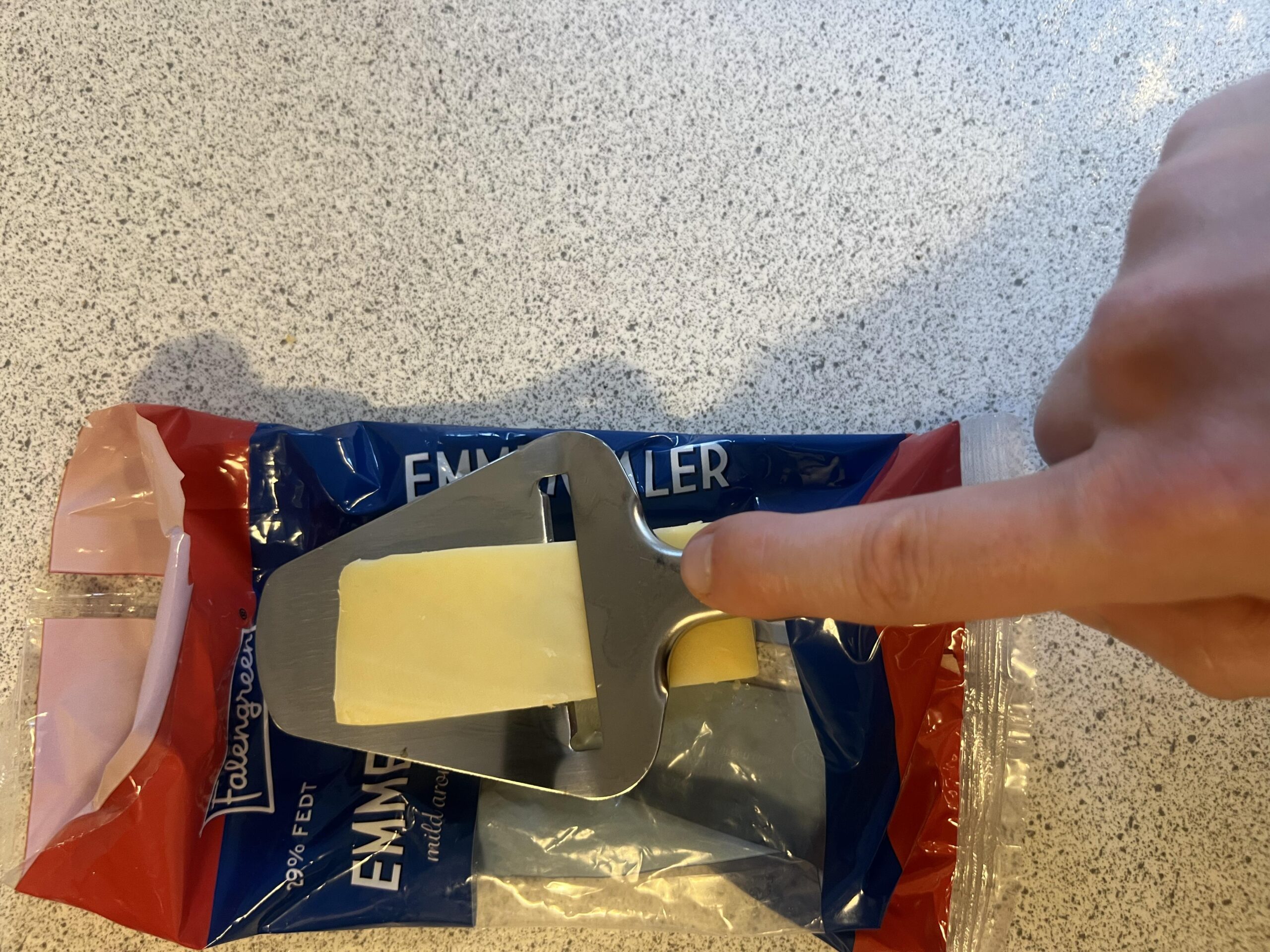 A thin Emmental cheese slice sitting on the blade of my LAMXD cheese slicer over its packaging