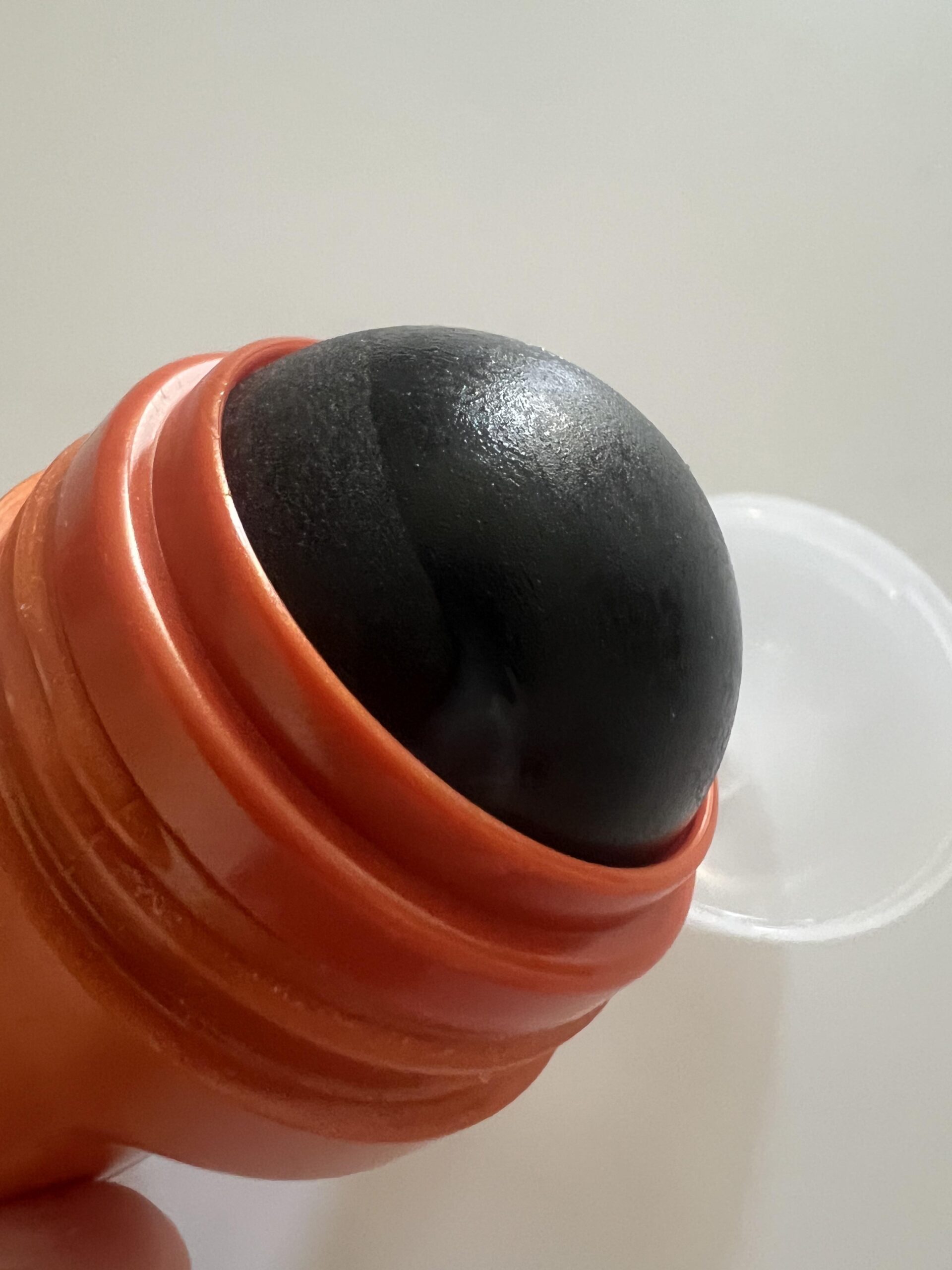 My close-up photo of the large black XXL roll-on ball on an orange L'Oréal Men Expert Heat Protect bottle with the clear cap beside it