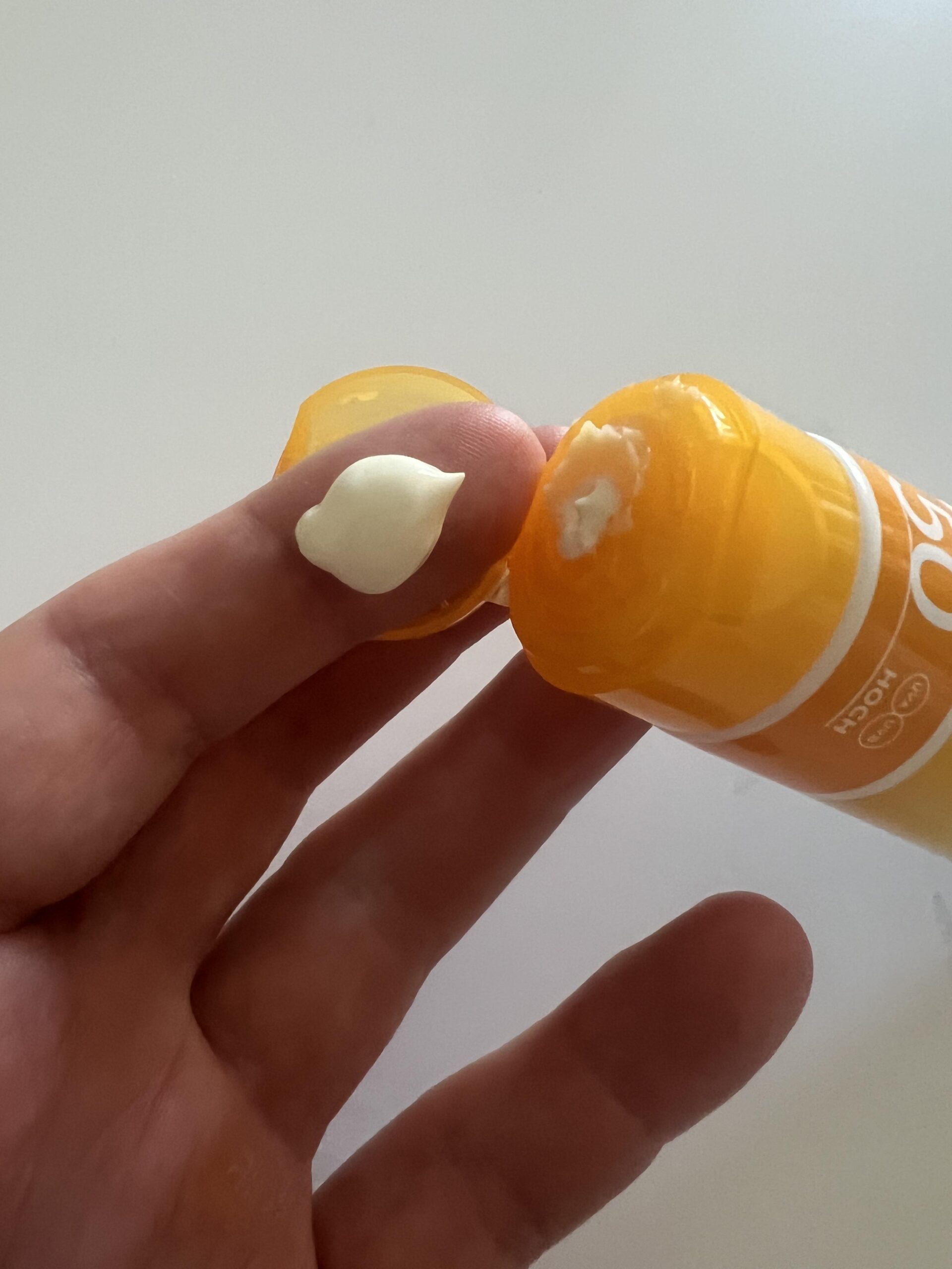 Original close-up of a dab of pale NIVEA SUN UV Face SPF 50 Q10 sunscreen on a fingertip beside the orange flip cap