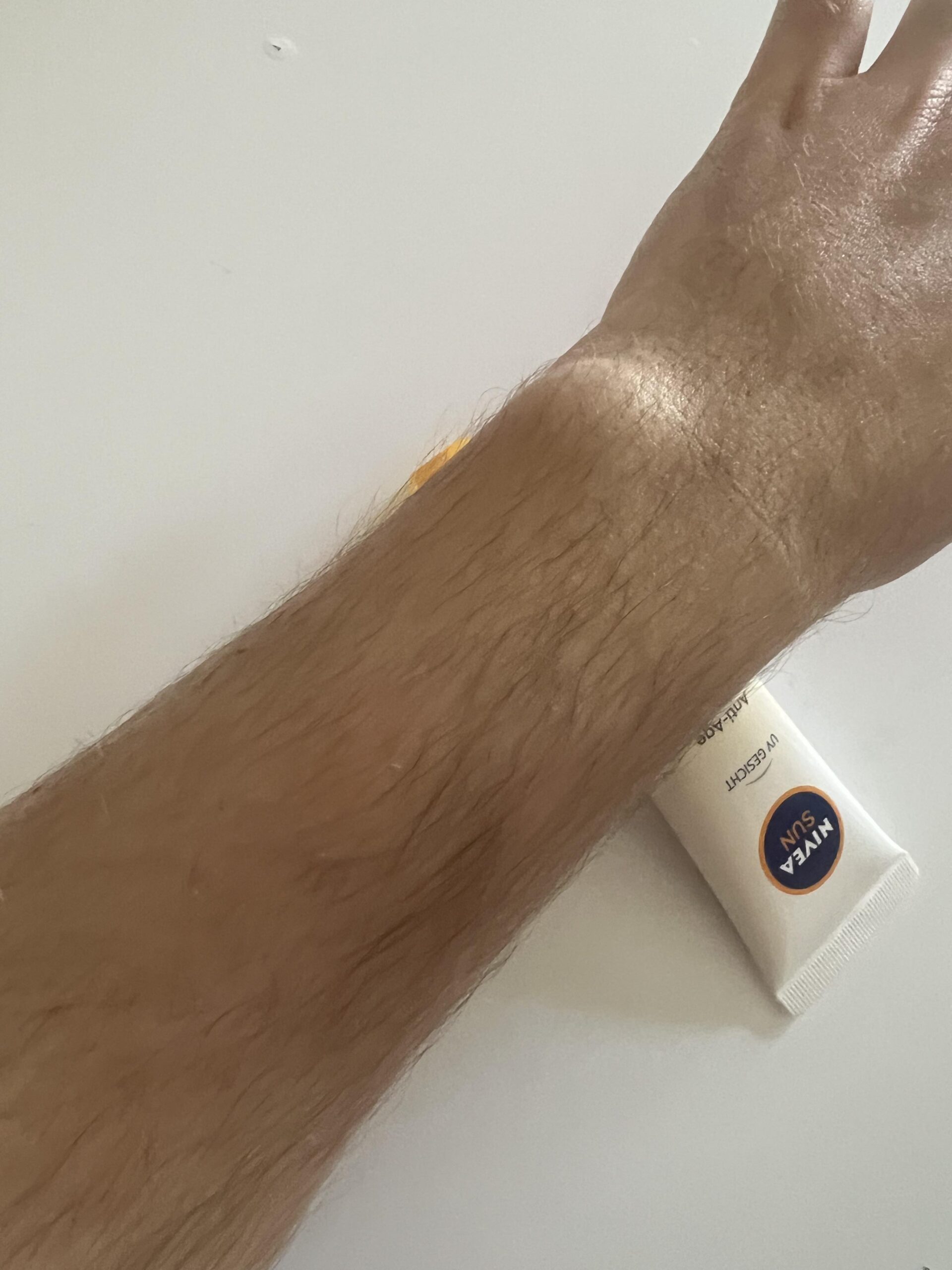 Original photo of a forearm after rubbing in NIVEA SUN UV Face Q10 SPF 50, with product tube nearby