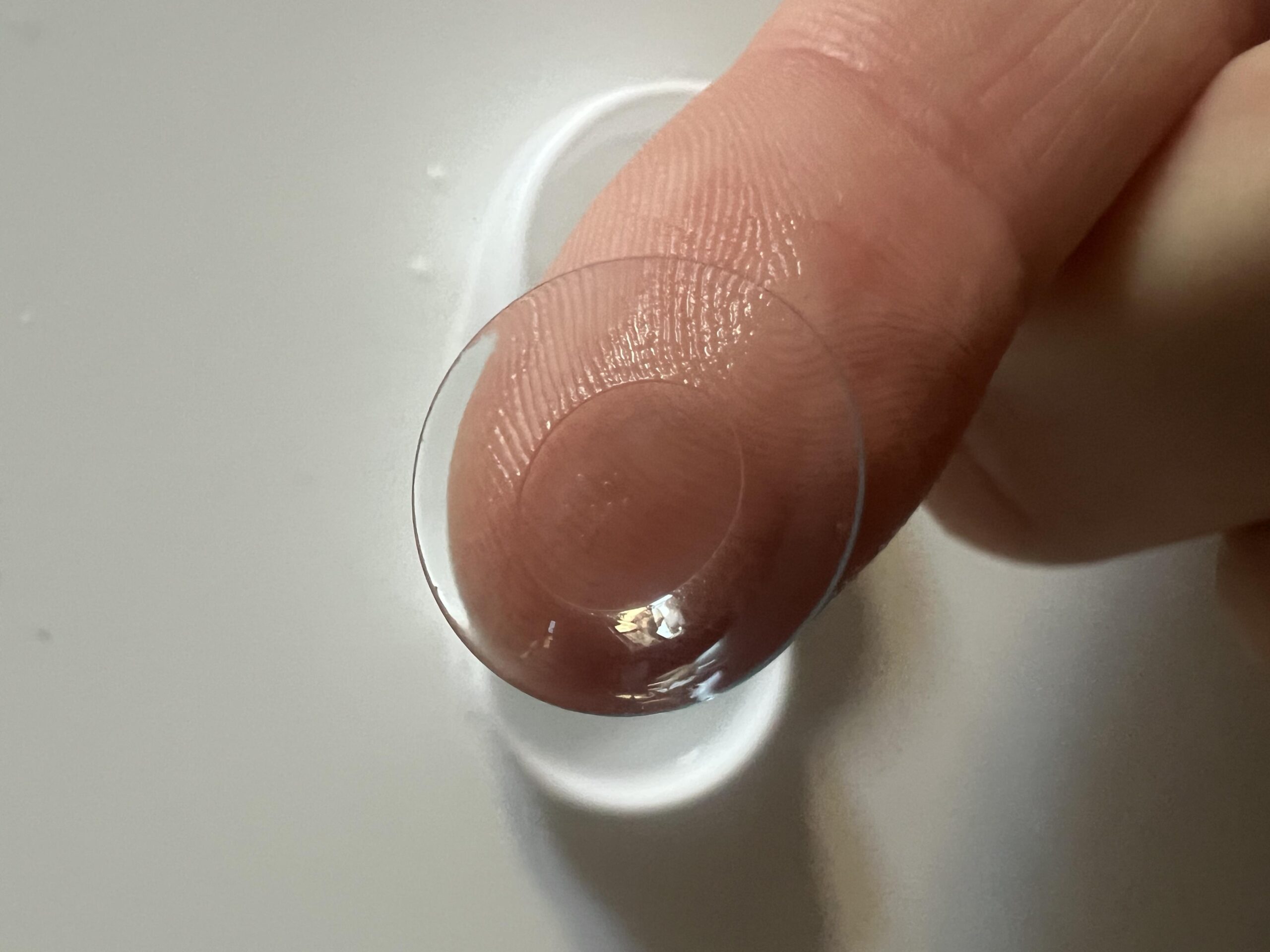Transparent soft TOTAL30 contact lens on a fingertip next to a lens case